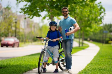 Baba ve oğul yaz tatilinde birlikte bisiklete biniyorlar. Mutlu bir baba ve heyecanlı bir çocuk hafta sonu bisiklet sürüyor. Sportif aile. Babalar Günü. Baba çocuğu eğitiyor ve destekliyor.