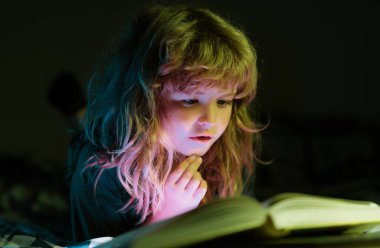 Çocuk uyumadan önce yatakta kitap okuyor. Evdeki küçük çocuk yatakta uzanıp kitap okuyor. Eğitim ve okuma kavramı