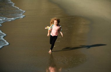 Sahilde oynayan çocuklar. Çocuklar yaz tatilinde denizde oynarlar. Kum ve su eğlencesi, güneş koruması. Koşmak ve çocuklar için sağlıklı spor