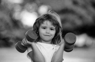 Spor portresi çocuklar. Fitness çocuğu. Parkda dambılı küçük bir çocuğun portresi. Jimnastik. Çocuk sporcusu, çocukluk aktivitesi. Çocuklar spor ve spor