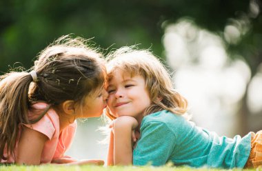 Portrait of cute boy and girl on summer field. Children in summer park. Cute kids face close-up. Playful little cute couple boy girl walk on meadow. Kids kiss and hug. Lovely children