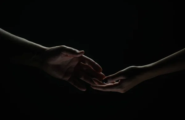 Two hands reaching toward. Helping hand outstretched for salvation on isolated black background. Close up of man and woman hand touch with fingers. Man and woman holding hands