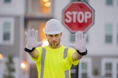 Jesti durduran, eli olmayan, konsept inşa etme konusunda tehlikeli bir mimar. Miğferli adam dur işareti gösteriyor. İnşaatçı dur diyor. İşçi üniformalı ve şapkalı bir adam dur işareti yapıyor.