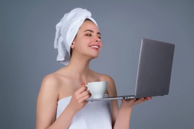 Morning freelancer working on laptop. Business woman with towel on head with coffee working on laptop. Morning coffee. Portrait of smiling woman with cup of coffee using laptop in gray studio