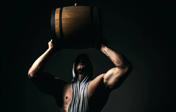 Muscular man wooden barrel on black. Brutal brewer man. Brewery concept. Beer for pub and bar. Oak barrels, keg. Man carries wooden barrel. Barrel with craft beer, whiskey, cognac or wine
