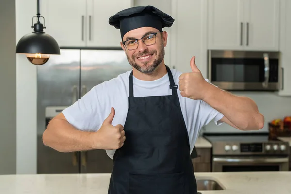 Happy chef cook with thumb up. Portrait of chef man in a chef cap in the kitchen. Man wearing apron and chefs uniform and chefs hat. Character kitchener, chef for advertising