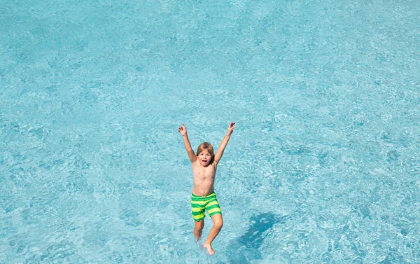 Child splashing in summer water pool. Kid splash in pool. Excited happy kid boy jumping in pool, water fun. Kid jumping in the swimming pool and splashing water. Kid splashing on poolside