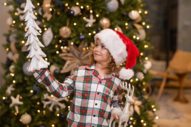 Mutlu çocuk bir Noel balosu düzenliyor. Çocuk bayramda, Noel 'de, Yeni Yıl' da seviniyor. Çocuk Noel ağacına karşı duruyor.