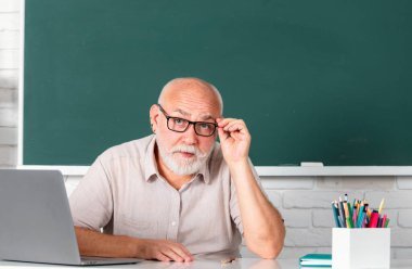 Grandfather education concept. Portrait of confident caucasian senior teacher in classroom. Middle aged man professor at high school