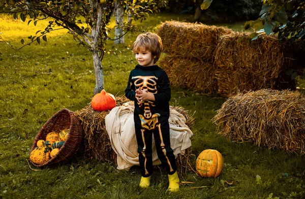 Halloween skeleton child. Boy sitting on the haystack. Little boy in skeleton costume playing in autumn park. Child outdoors in nature. Little child have fun on fresh air