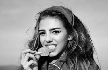 Gülümseyen kadın patates cipsi yiyor. Dişleriyle patates cipsi yiyen genç bir kadın. Lezzetli fast food. Cips yiyorum. Abur cubur yiyen tatlı bir kadın. Fast food seksi kadın model.