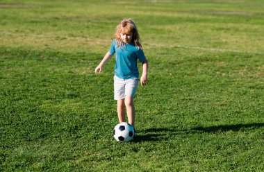 Genç futbolcu. Genç çocuk futbol topunu tekmeliyor. Futbolcu hareket halinde, çocuk hareket halinde. Spor yaparken tatlı bir çocuk.