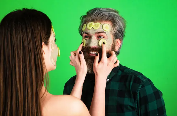 Man facial cucumber. Funny couple with a clay mask. Male bearded model and female model with clay mask on the face