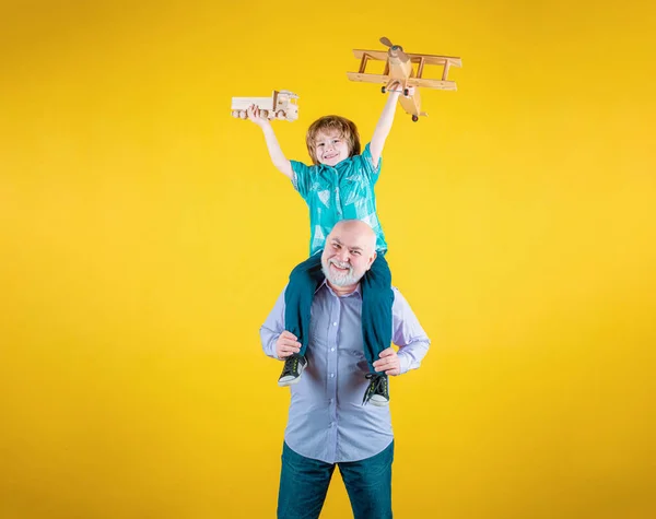 Grandfather and grandson piggyback ride with plane and wooden toy truck. Men generation granddad and grandchild