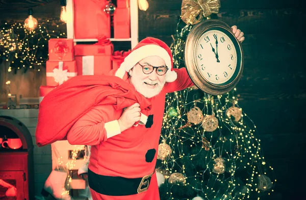 快乐的圣诞老人手持着壁炉和圣诞树背景上的闹钟 圣诞老人在家里 圣诞老人在圣诞树背景下拿着闹钟 — 图库照片