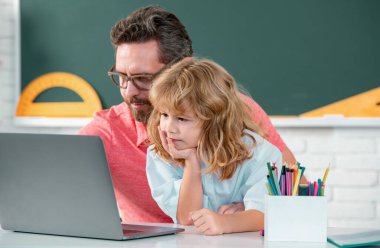 Dizüstü bilgisayarda öğrenen bir okul çocuğu olan öğretmen, online eğitimle çalışıyor. Öğretmen ve öğrenciler sınıfa. İlkokuldan çocuk öğrenciye yardım eden öğretmen