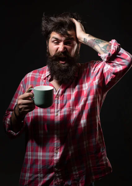Mans holds cup of coffee and yawning on black. Morning tea. Yawning face. Man with tea cup. Hipster man yawning with cup of coffee. Bearded man yawning hold mug tea. Wake up. Happy day. After morning