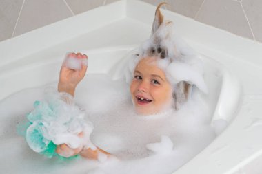 Çocuk kafasında sabun. Köpüklü çocuk yüzü. Banyo köpüğüyle yıkanan çocuk. Tatlı çocuk banyo yapar, beyaz bir banyoda sabun köpüğü ve şampuanla yatar.