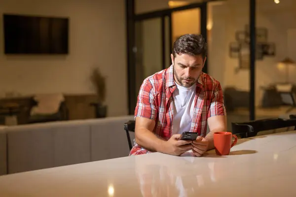 Handsome man with mobile phone sitting on weekend at home. American man using phone while sitting on sofa at living room interior. Relaxing text with smartphone. Call phone