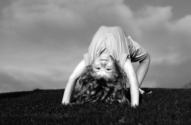 Çocuk yaz parkında yeşil çimlerin üzerinde baş aşağı duruyor. Sağlıklı aile hayatı kavramı. Eğlenceli ve tasasız bir çocukluk. Çocuklar doğada spor yapar.