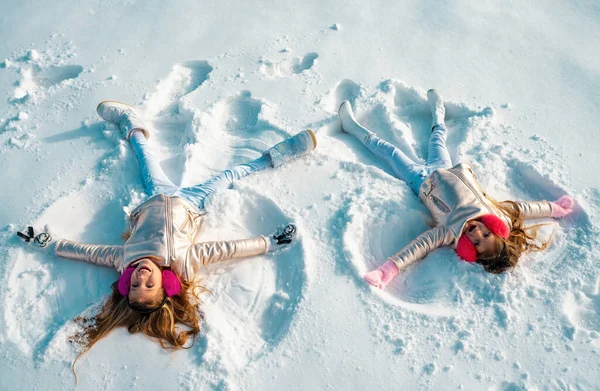 Two Girls on a snow angel shows. Children playing and making a snow angel in the snow. Top view
