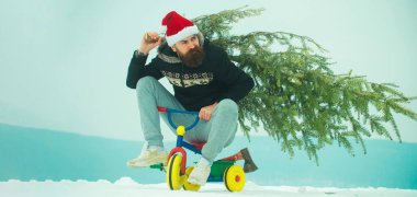 Bisikletli komik bir adam Noel ağacını önemsiyor. Kışın arka planda kardan adam. Kış bayrağı için kardan adam. Çocuk bisikleti üstünde komik bir baba Noel ağacı tut