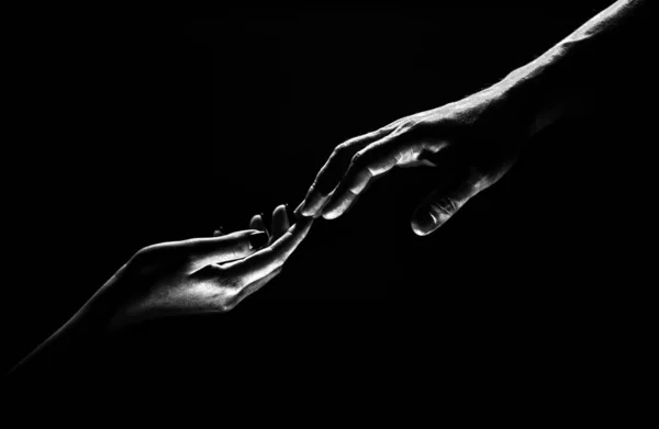 Hands gesturing on black background. Giving a helping hand. Support and help, salvation. Hands of two people at the time of rescue. Romantic touch with fingers, love. Hand creation of adam