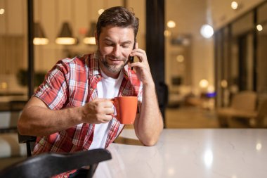 Serbest çalışan bir iş adamı cep telefonu kullanıyor sosyal medyayı kontrol ediyor ya da evde mesajlaşma sohbeti yapıyor. İnternette evden çalışıyor. Adam oturma odasında sıkı çalışma gününden sonra dinleniyor. Evdeki koltukta cep telefonu kullanan adam.