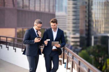 Çevrimiçi para işlemleri, mobil ödemeler. Takım elbiseli iki iş adamı dışarıda kredi kartı ve laptop tableti tutuyor. Hesabı öde. İşadamları tabletle ödeme yaparken kredi kartı tutuyorlar