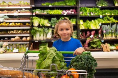 Markette alışveriş arabası ve sebzeli çocuk. Çocuklarla alışveriş. Çocuk süpermarketten meyve alıyor. Küçük çocuk marketten taze sebze alır. Çocuk sebze seçiyor. Sağlıklı yemek.