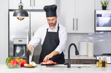 Aşçı mutfakta sebzelerle yemek pişiriyor. Sağlıklı yemek. Mutfakta yemek pişiren çekici beyaz adam. Modern mutfakta sağlıklı yemek pişiren adam. Şef mutfakta yemek hazırlıyor.