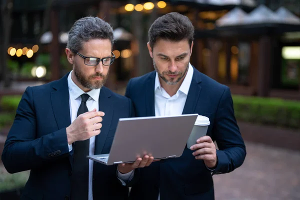 Two businessman using laptop outdoor. Businessmen discussing a presentation on laptop. Business project. Successful business. Businessman presenting new business idea on laptop
