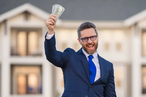 Portrait business man holding cash dollar bills front of house outdoor. Big luck. Dollar cash money concept. Rejoices to win cash. Man hold cash money. Financial luck and success. Manager or realtor