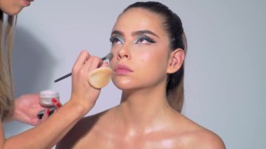 Profesyonel makyöz güzel genç bir kadınla çalışıyor. Genç manken için makyajı kapat. Makyaj sanatçısı makyaj yapıyor. Profesyonel makyöz, cazibe modeli makyajı yapıyor.