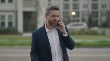 Sokakta yürüyen ve telefonla konuşan kendine güvenen bir iş adamının portresi. Olgun bir iş adamı dışarıda telefonla konuşuyor. Telefon kullanan resmi takım elbiseli bir iş adamı.