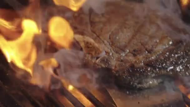 火の炎でローストビーフ 火でグリルにビーフステーキ リブアイステーキ 燃えるグリルで調理 サーロインステーキの炎がバーベキューで燃え上がった グリルにステーキ バーベキューで焼いた肉 — ストック動画