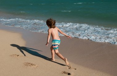 Çocuk yaz tatilinde plajda oynuyor. Doğadaki çocuklar, deniz suyunda akan kumlar ve mavilikler.