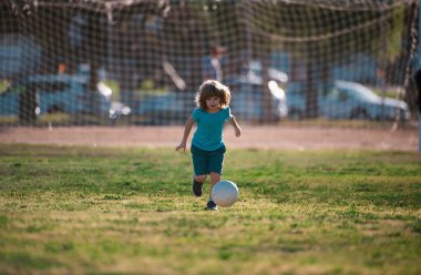 Dışarıdaki çimlerde top oynayan heyecanlı çocuk. Futbolcu çocuklar, çocuklar futbol oynar. Çocuk sahada futbol oynuyor.