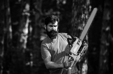 Ormanın yakınında baltası olan yakışıklı bir genç. Ormanların yok edilmesi. Tahta testereli baltayla ormanda oduncu. Tarım ve ormancılık teması