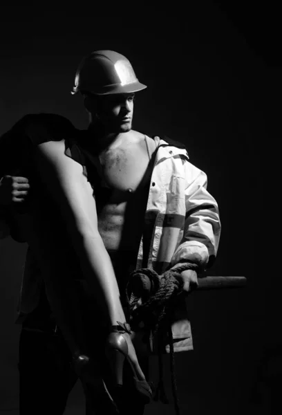 Having a strong sexual appeal in constructor uniform. Muscular man in worker uniform holding sexy woman. Handsome man dressed like constructor or miner, uniform fetish. Uniform fetishism.