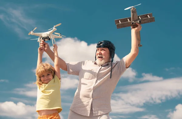 Young grandson and old grandfather playing with toy plane and quadcopter drone against sky. Child pilot aviator with plane dreams of traveling. Family Relationship Grandfather and child