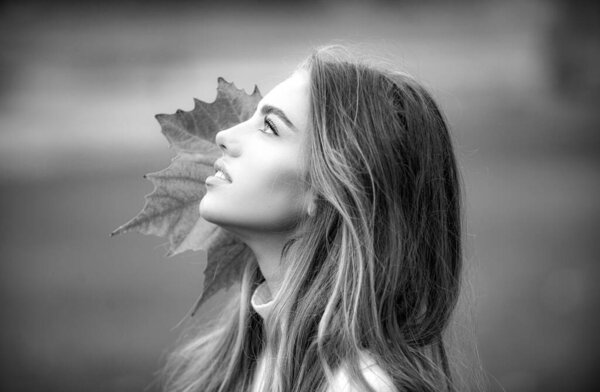 Fashion autumn face of Beautiful woman with leaf. Beauty girl outdoors enjoying nature