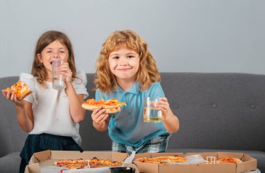 Cute little boy and girl eating Pizza at home. Children holding a slices of pizza on party at home. Little girl and boy eat pizza