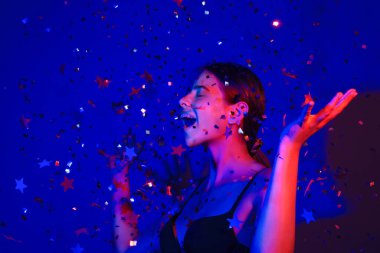 Doğum günün kutlu olsun. Konfeti üfleyen kızın stüdyo portresi. Doğum günü ya da sevgililer günü için konfeti. Seksi model doğum gününde konfeti üflüyor. Doğum günü esprilerini kutlayan şehvetli kadın.