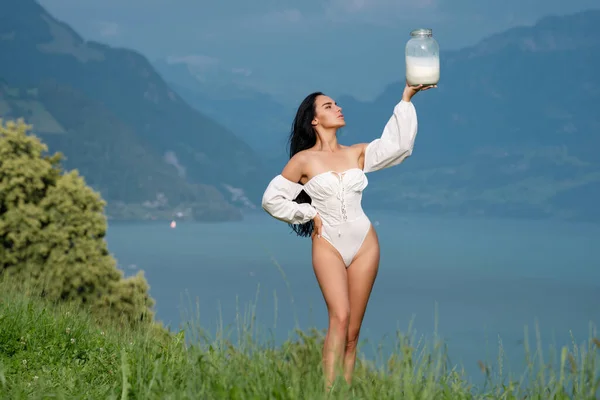 Beautiful woman enjoys milk on alpine village in the mountains. Beauty romantic girl drink milk outdoors. Model drink Milk at a picnic on Alpine meadow. Girl with a bottle of fresh milk in the village