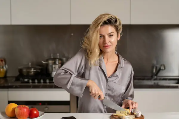 Sexy woman preparing food, cutting cheese and sausage in the kitchen. Woman wearing sexy pajama cooking breakfast in home kitchen