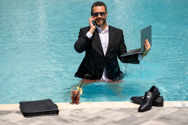 Freelance work, distance online work, e-working. Summer business. Business man in suit remote working on laptop in pool. Business man working online on laptop in summer swimming pool water
