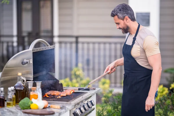 BBQ, grilling, barbecue outside. Man with barbeque roast fish outdoor. Grilling and barbecue concept. Bbq and grill. Man in barbecue preparing fish salmon. Chef cooking barbecuing seafood