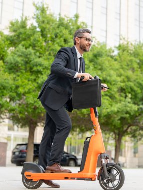 İşadamı elektrikli scooterıyla havalı ve modaya uygun görünüyor. Ekolojik ve hızlı. Elektrikli scooter kullanan yakışıklı bir iş adamı. Hızlı iş toplantısı. İş adamı, zaman ve para her gün işe gidip geliyor.