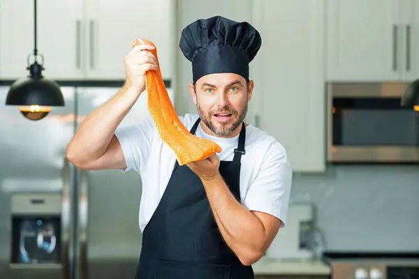 Handsome man cooking fish salmon in kitchen. Portrait of casual man cooking in the kitchen with salmon fish. Casual man preparing raw fish salmon in kitchen. Chef with big salmon steak